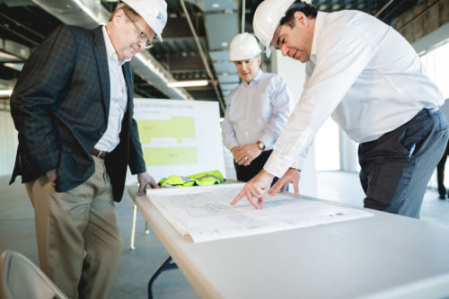 three men in white hard hats looking at blue print on table